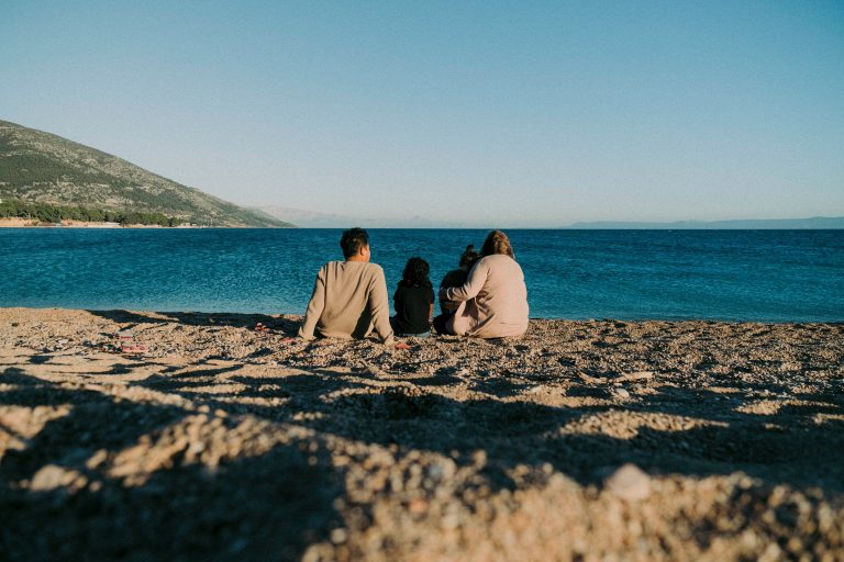 a group of people sitting on a beach looking at the water