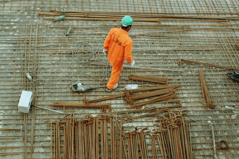 a man in orange jumpsuit and green hard hat standing on a steel grid