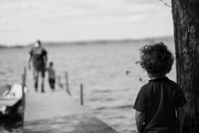 a child looking at a man fishing on a dock